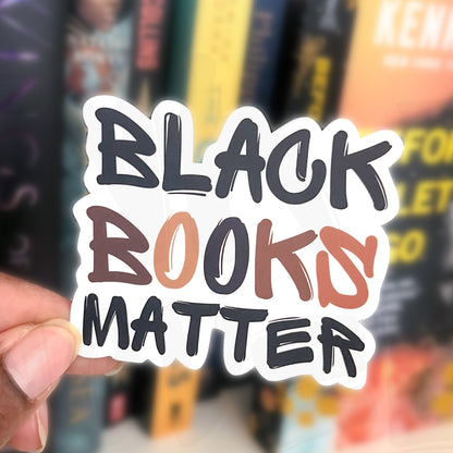 Hand holding a 'Black Books Matter' sticker with books in the background